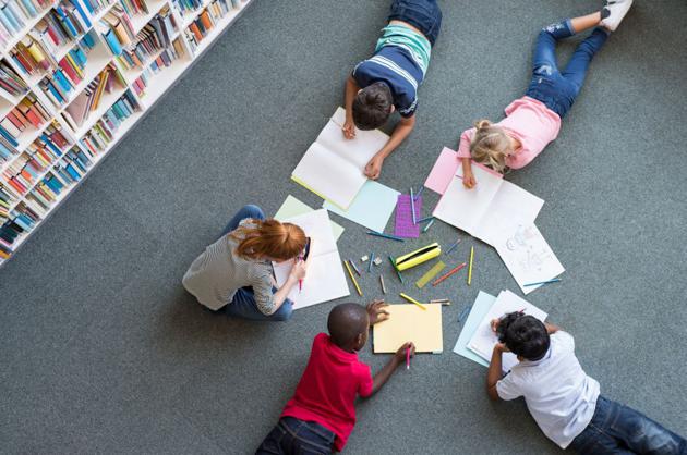 Abbildung: Kinder, die in einer Bibliothek auf dem Boden liegen und in Hefte schreiben
